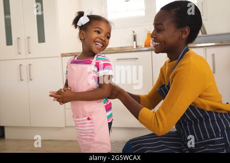 Lächelnde afroamerikanische Mutter und Tochter, die Spaß in der Küche haben, Schürzen zum Backen aufsetzen Stockfoto