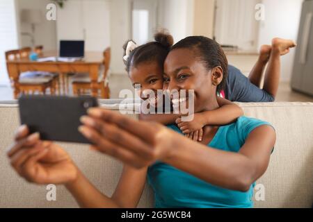 Lächelnde afroamerikanische Mutter und Tochter entspannen sich auf der Couch und machen Selfie Stockfoto