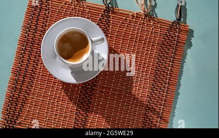 Frisch gebrühter Morgenkaffee, auf einer Bambusplatte und auf dem hellblauen Farbtisch mit Schnittmarken, harten Schatten, Draufsicht Stockfoto