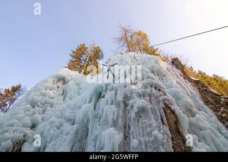 Eiskletterin, die an einem Seil hängt und den Platz wechselt, indem sie auf einen eisgefrorenen Wasserfall springt Stockfoto