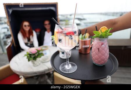 30. Juni 2021, Mecklenburg-Vorpommern, Kühlungsborn: Auf der Terrasse des Restaurants Vielmeer am Bootshafen serviert Ibrahim Hussein Gäste, die in einem Strandstuhl sitzen. Der Neubeginn von Gastronomie und Tourismus nach monatelanger Corona-Zwangspause hat dem Arbeitsmarkt in Mecklenburg-Vorpommern einen starken Schub gegeben. Für den Monat Juni meldete die Nord-Regionaldirektion der Bundesagentur für Arbeit in Kiel am Mittwoch bundesweit 61,600 Arbeitslose. Das waren 4800 weniger als im Vormonat Mai und 4300 weniger als im Juni 2020. Foto: Bernd Wüstneck/dpa-Zentralbild/dpa Stockfoto