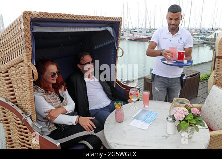 30. Juni 2021, Mecklenburg-Vorpommern, Kühlungsborn: Auf der Terrasse des Restaurants Vielmeer am Bootshafen serviert Ibrahim Hussein Gäste, die in einem Strandstuhl sitzen. Der Neubeginn von Gastronomie und Tourismus nach monatelanger Corona-Zwangspause hat dem Arbeitsmarkt in Mecklenburg-Vorpommern einen starken Schub gegeben. Für den Monat Juni meldete die Nord-Regionaldirektion der Bundesagentur für Arbeit in Kiel am Mittwoch bundesweit 61,600 Arbeitslose. Das waren 4800 weniger als im Vormonat Mai und 4300 weniger als im Juni 2020. Foto: Bernd Wüstneck/dpa-Zentralbild/dpa Stockfoto