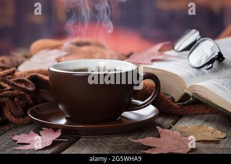 Nahaufnahme einer Tasse heißen Kaffee und Buch auf einem Holztisch im Freien mit herbstlichem Hintergrund Stockfoto