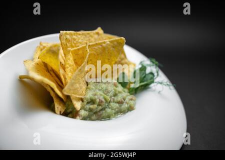 Nahaufnahme von Guacamole Dip in Schüssel mit Avocado und Nachos auf schwarzem Hintergrund Stockfoto