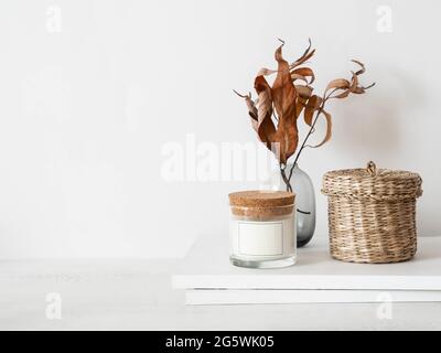Gemütliches Herbsthaus Stillleben von trockenen Herbst Zweige in Vase, weiße Glaskerze, Weidenbox und Zeitschriften auf weißem Tisch. Vorderansicht. Speicherplatz kopieren Stockfoto
