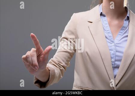 Mittelteil der kaukasischen Geschäftsfrau berührt virtuelle Schnittstelle auf grauem Hintergrund Stockfoto