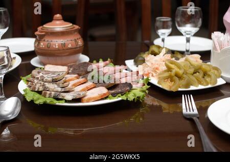 Fleischvorspeise mit geräuchertem putenfleisch, Rindfleisch, Pferdefleischwurst und Gurken, grünen gesalzenen Tomaten, Sauerkraut stehen auf dem Banketttisch Stockfoto