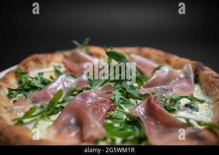 Nahaufnahme der italienischen Pizza mit Prosciutto, Rucola und Käse auf schwarzem Hintergrund Stockfoto