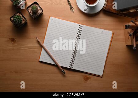 Draufsicht leeres Notizbuch, Bleistift, Kaffeetasse und Kaktus auf Holzschreibtisch. Stockfoto