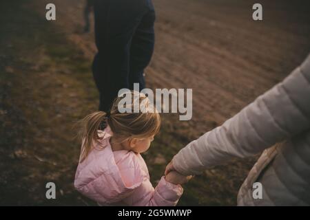Die Eltern halten die Hände ihrer Tochter für einen Spaziergang. Stockfoto
