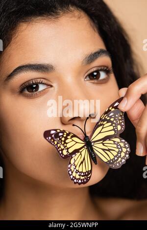 Nahaufnahme einer afroamerikanischen jungen Frau mit Schmetterling auf Lippen isoliert auf Beige Stockfoto