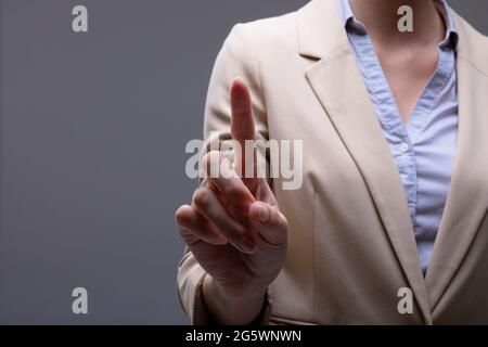 Mittelteil der kaukasischen Geschäftsfrau berührt virtuelle Schnittstelle auf grauem Hintergrund Stockfoto