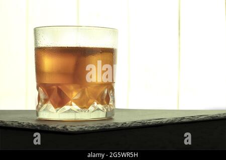 Vernebeltes Glas mit Wassertropfen und Whiskey mit Eis. Verschwitztes Glas Whiskey mit Eis auf dem Tisch mit Kopierfläche Stockfoto