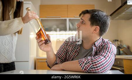 Junge Frau, die eine Flasche Alkohol von männlichen alkoholischen Spirituosen in der Küche nimmt Stockfoto