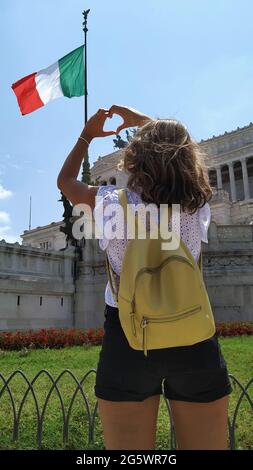 Junge Frau, die sich mit den Händen auf die Flagge italiens zugewandt herzförmig macht Stockfoto