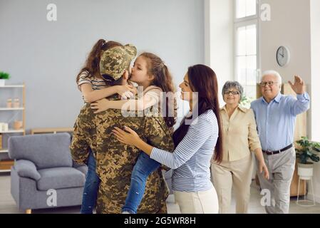 Emotionales Porträt eines unkenntlichen Mannes in Militäruniform, der seine große Familie umarmt. Stockfoto