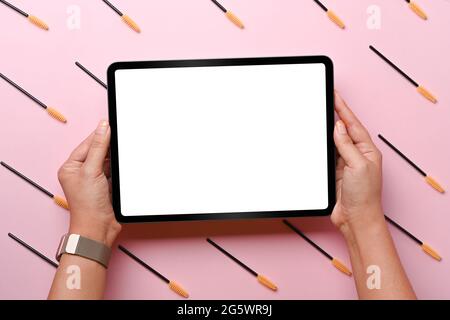 Frau hält digitale Tablette mit Augenbraue und Wimpern Pinsel auf rosa Hintergrund. Stockfoto