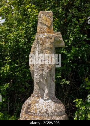 Eine stark beschädigte Statue von zwei Figuren, einem Christus am Kreuz auf einer Steinsäule am Straßenrand in der Nähe von Bruisyard Hall, Suffolk, Großbritannien Stockfoto