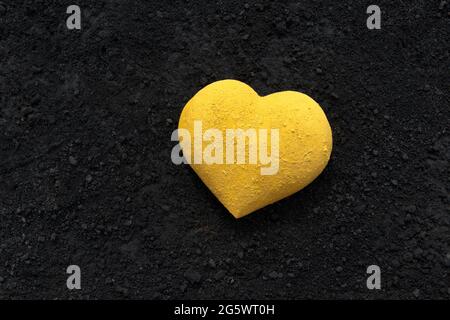 3 dimensionale Herzform, leuchtend gelb mit Pulverfarbe gemalt, auf einem Hintergrund aus schwarzen Bindemitteln platziert Stockfoto