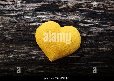 3 dimensionale Herzform, gelb gestrichen und mit trockenem Pigment bestreut, auf dem Hintergrund verwittertem Holz. Stockfoto