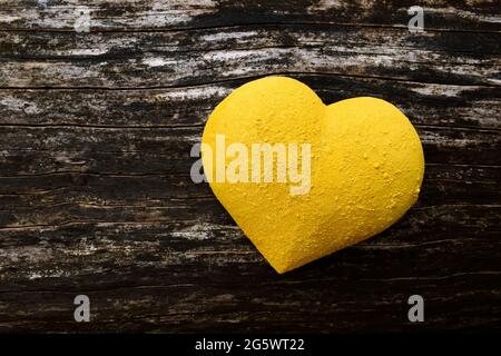 3 dimensionale Herzform, gelb gestrichen und mit trockenem Pigment bestreut, auf dem Hintergrund verwittertem Holz. Stockfoto