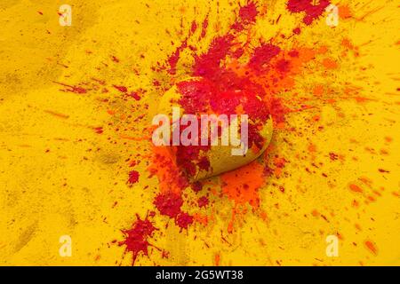 Gelbes Herz auf gelbem Hintergrund, mit oranger und roter Farbe bespritzt. Stockfoto