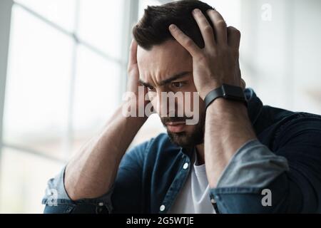 Trauriger und besorgter Mann sitzt auf der Couch und fühlt negative Emotionen, Depressionen und Probleme Stockfoto