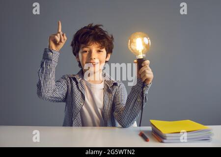 Porträt eines klugen Jungen, der eine helle Glühbirne hält und seinen Finger nach oben hebt und eine tolle Idee hat. Stockfoto