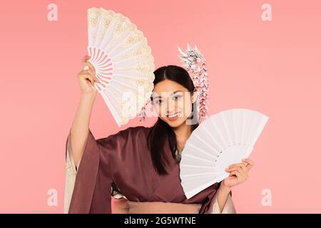 Lächelnde asiatische Frau hält Fans isoliert auf rosa Stockfoto