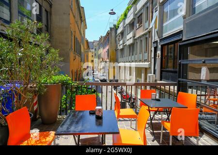 Schwarzer Tisch mit orangefarbenen Stühlen über Pflanzen, farbenfrohe Gebäude auf der Restaurantterrasse. Straßencafé außen. Stadtleben Stockfoto