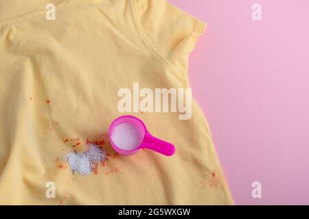 Flecken auf der Kleidung. Waschpulver in einem Plastiklöffel. Entfernung von Flecken von verschütteten Getränken. Trockenreinigungskonzept. Hochwertige Fotos Stockfoto