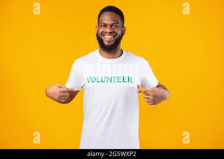 Glücklicher afroamerikanischer Freiwilliger, der sein T-Shirt auf gelbem Hintergrund zeigt Stockfoto