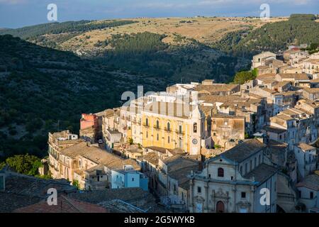 Ragusa, Sizilien, Italien. Blick über die malerischen Dächer von Ragusa Ibla, Sonnenuntergang, Häuser, die sich an einem steilen Hang über einer bewaldeten Schlucht Klammern. Stockfoto