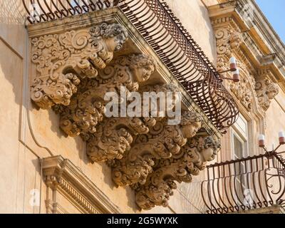 Noto, Syrakus, Sizilien, Italien. Fein geschnitzte Steinfiguren, die einen dekorativen Balkon auf der barocken façade des Palazzo Nicolaci di Villadorata stützen. Stockfoto