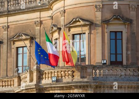 Noto, Syrakus, Sizilien, Italien. Die Flaggen Siziliens, Italiens und der Europäischen Union, die vom Balkon des Palazzo Ducezio, dem heutigen Rathaus, fliegen. Stockfoto