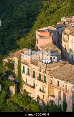 Ragusa, Sizilien, Italien. Blick über die malerischen Dächer von Ragusa Ibla, Sonnenuntergang, Häuser, die sich an einem steilen Hang über einer bewaldeten Schlucht Klammern. Stockfoto