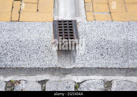 Drain Rost-System, Grill für die Entfernung von Regenwasser von Wanderwegen durch Graben und Loch in Granit-Randstein auf der Straße schließen, niemand. Stockfoto