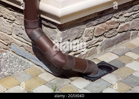 Dachrinne aus braunem pvc-Kunststoff Ableitung des Regenwassers vom Dach des Hauses in das Bodenentwässerungssystem an der Fassade des Gebäudes ausgekleidet Stockfoto