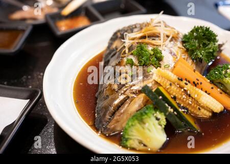 Lachs-Kabutoni mit japanischer Sauce und gekochtem Gemüse auf weißem Gericht. Stockfoto