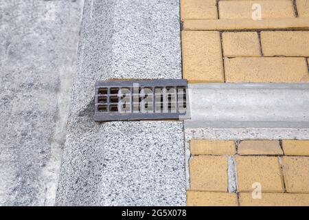 Drainage-System Gitter, Grill für die Entfernung von Regenwasser von Gehsteig durch Graben und Loch in Granit Curbe auf der Straße Nahaufnahme Seitenansicht, n Stockfoto