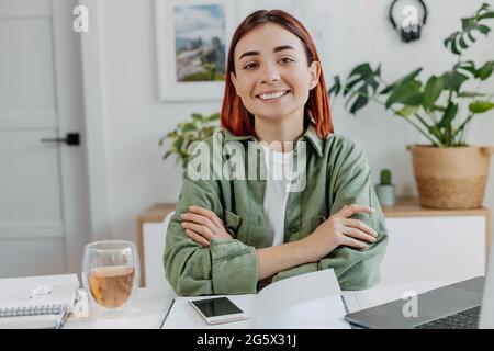 Porträt einer lächelnden jungen Frau, die zu Hause mit einem Laptop arbeitet. Entspannte Geschäftsfrau mit einer Tasse Tee. Konzept des Online-Geschäfts oder der Kommunikation, freel Stockfoto