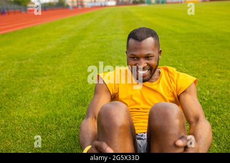 Nahaufnahme Porträt eines gesunden jungen Afro-amerikanischen schwarzen Mannes, der im Stadion knirscht, seinen Körper fit hält und Aufwärmübungen macht Stockfoto