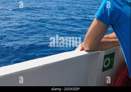 Junger Mann, der sich auf das Geländer einer Passagierfähre lehnt und auf das Meer blickt Stockfoto