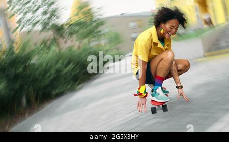 Afroamerikanische Frau mit Vitiligo begeistert mit Skateboarding auf der modernen Stadtstraße. Unscharfer Fokus Stockfoto