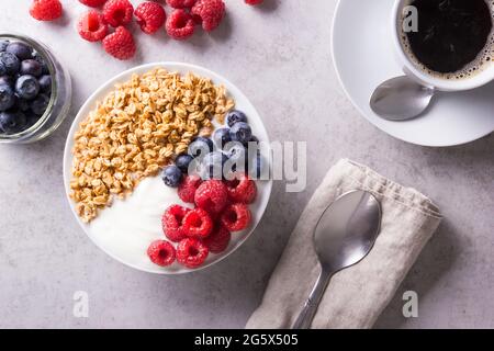 Das Frühstück besteht aus einfachem Joghurt, garniert mit Beeren und Müsli-Haferbrei neben einer Tasse Kaffee Stockfoto