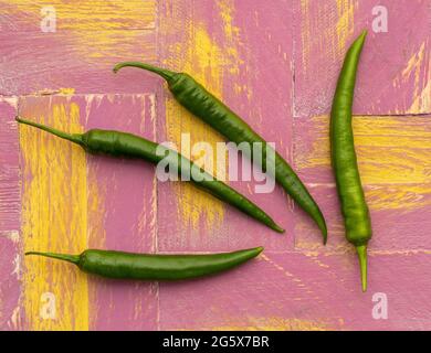 Grundrisse grüne Chilischoten auf einem rosa-gelben, hölzernen Hintergrund. Stockfoto