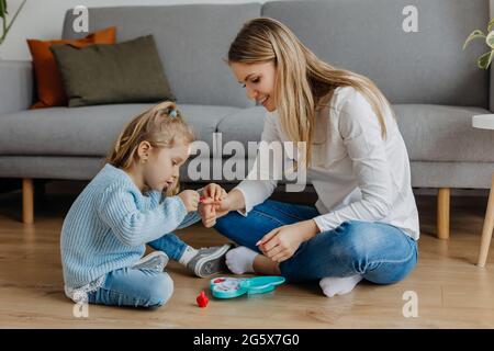 Mutter und kleine Tochter malen ihre Nägel mit Spielzeug-Nagellack. Kind spielt mit Mutter zu Hause. Konzept der guten Elternschaft und glückliche Kindheit, Familie