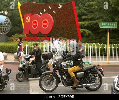 Peking, China. 30. Juni 2021. Autofahrer warten am Mittwoch, dem 30. Juni 2021, an einer Kreuzung neben einer Plakatwand zum Gedenken an den 100. Jahrestag der Kommunistischen Partei Chinas in Peking. China begeht diese Woche den hundertsten Jahrestag seiner regierenden Kommunistischen Partei, indem es seinen wachsenden Einfluss im Ausland ankündigt, zusammen mit dem Erfolg bei der Bekämpfung von Korruption und Armut im eigenen Land. Foto von Stephen Shaver/UPI Credit: UPI/Alamy Live News Stockfoto