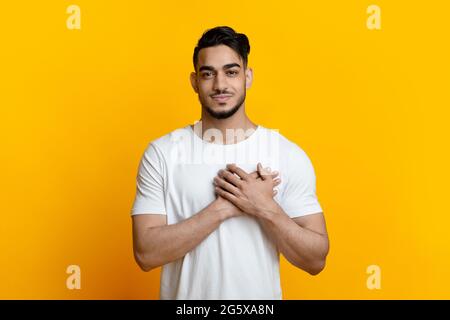 Lächelnder arabischer Kerl, der Handflächen auf der Brust hält Stockfoto