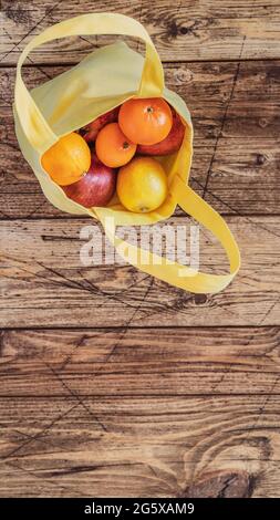 Vertikales Banner mit natürlichen Früchten: Zitronen, Orangen, Grapefruit und Granatäpfel in einem gelben Baumwollbeutel auf einem Holzhintergrund. Umweltfreundliches Einkaufen Stockfoto